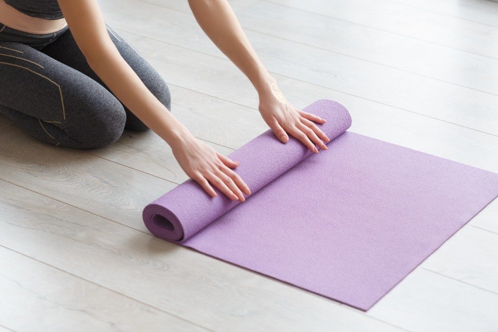 Woman rolling her lilac mat after a yoga class on wooden floor