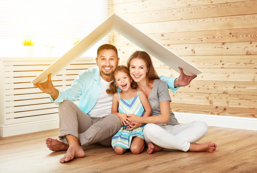 A family holding a cardboard to resemble a roof indoors