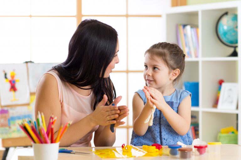 mother talking and teaching young daughter in play room using clay