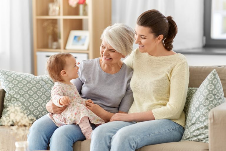 grandma holding baby girl with mother smiling beside them in the couch